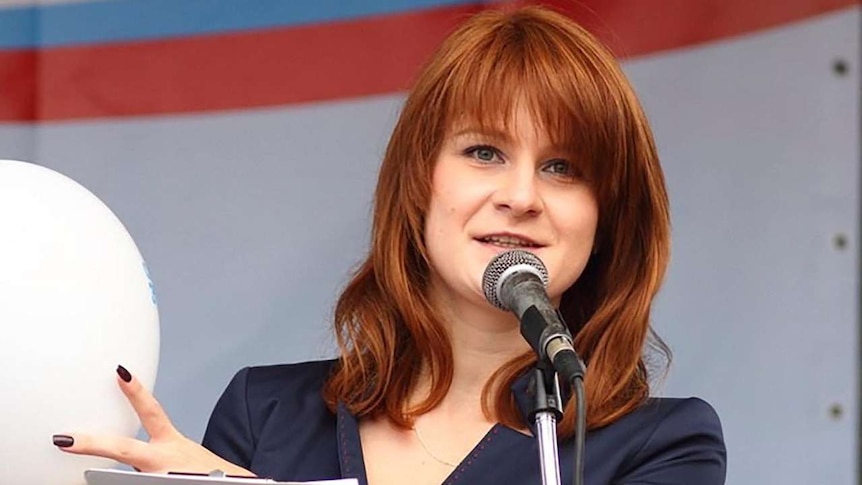 A red-haired woman smiles at the camera while pointing to a white ball in her hand
