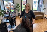 Woman standing at a hairdressing seat with a client, smiling. 