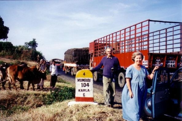 Two people stand near a milestone in India.