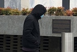 A man wearing all black walks out of an official building.