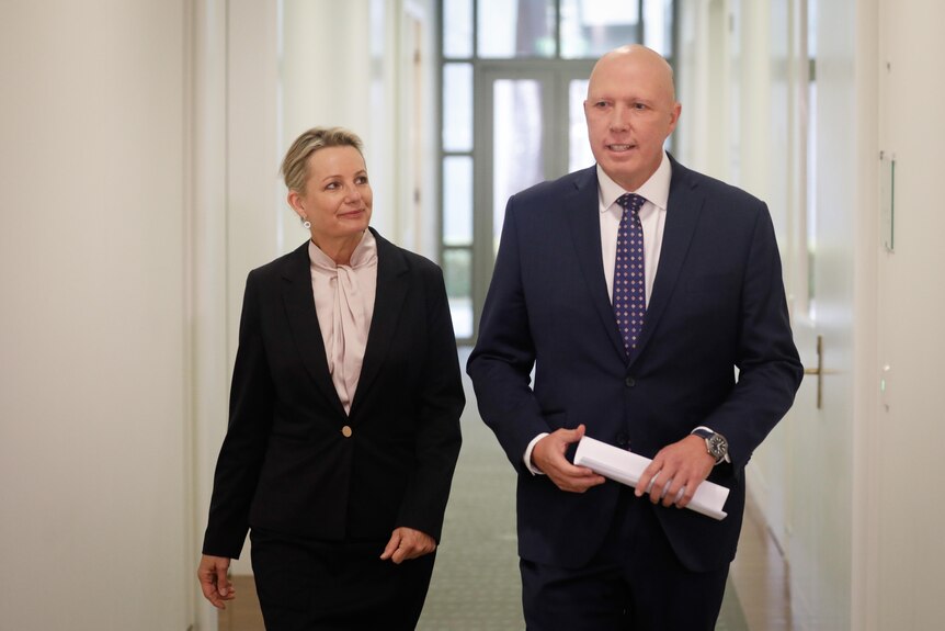 Ley is looking at Dutton as they walk through a corridor. Dutton is smiling.