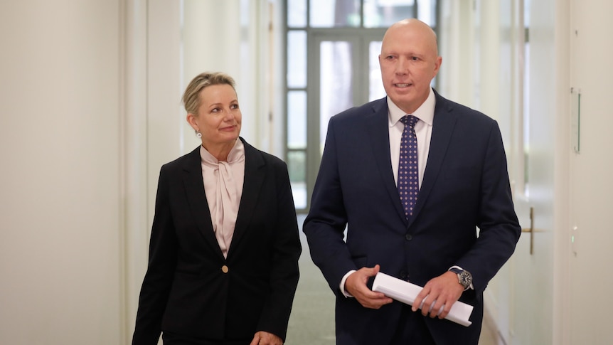Ley is looking at Dutton as they walk through a corridor. Dutton is smiling.