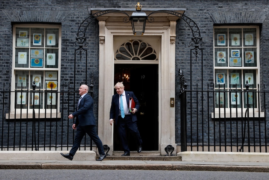 Johnson iese pe ușa din Downing Street ținând un dosar. 