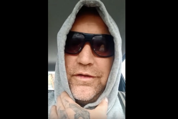 a man in a grey hoodie with dark glasses. his hand has tattoos on it.