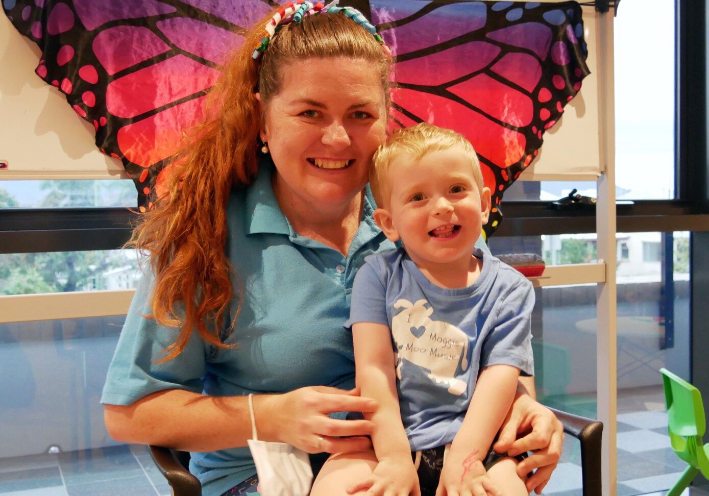 A woman with a toddler on her lap, both smile at the camera