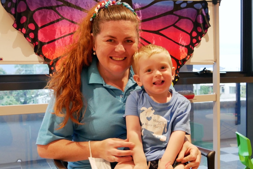 A woman with a toddler on her lap, both smile at the camera