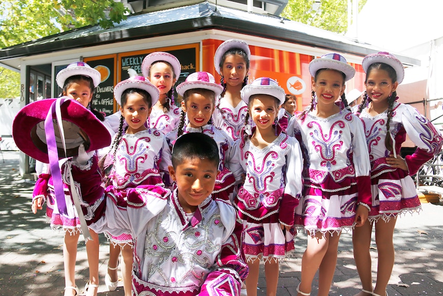 A group of children wearing pink and white costumes stand and pose for the camera.
