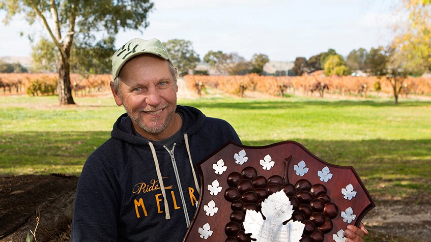 The Barossa's Steve Schiller holding the prestigious SA Pruning champion's Wolf Blass Shield in a vineyard.