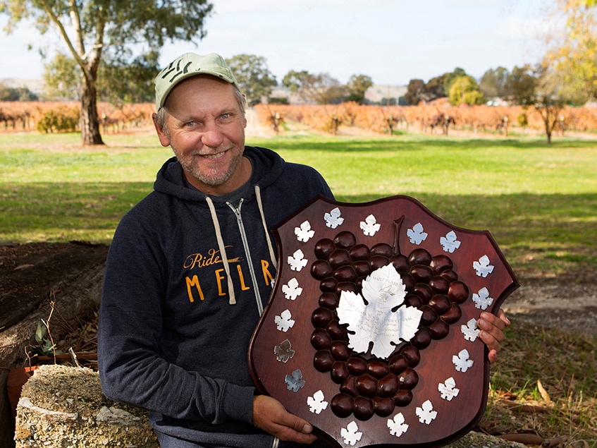 The Barossa's Steve Schiller holding the prestigious SA Pruning champion's Wolf Blass Shield in a vineyard.