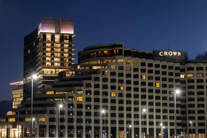 Tall buildings in the dark with lights on with an illuminated sign with the word Crown below a crown symbol.