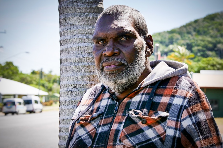 Aboriginal man standing in front of tree on side of street looks at camera