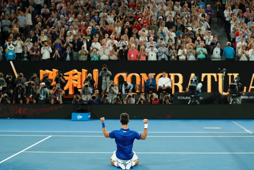 Novak Djokovic on knees pumping his arms in front of the Rod Laver Arena crowd.