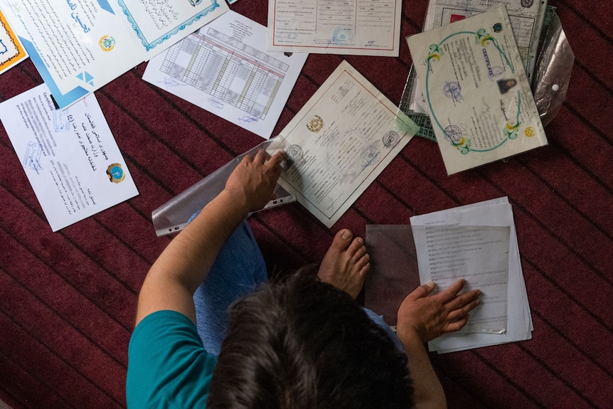 Taken from above, a man sits on the ground among all his paperwork. 