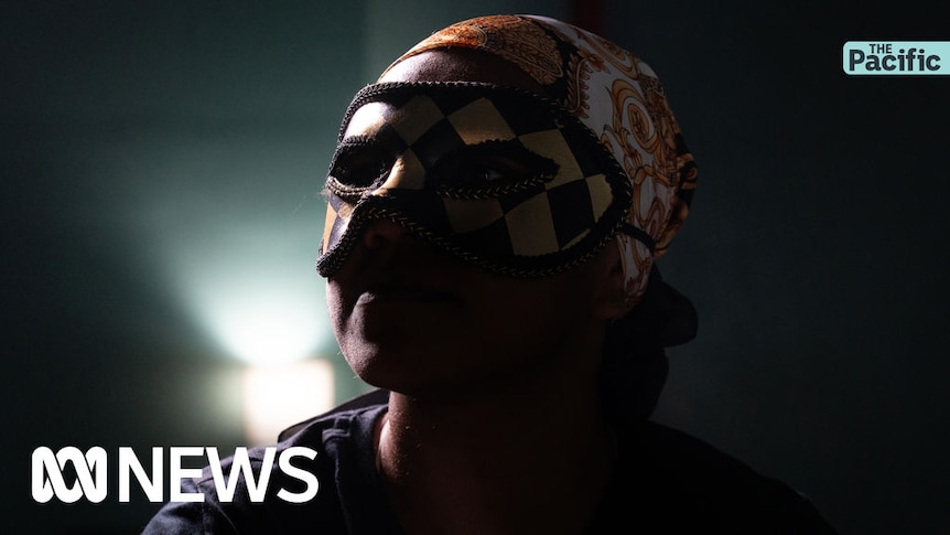 The Pacific: A woman with an ornate black and gold mask and bandana in a darkened room.
