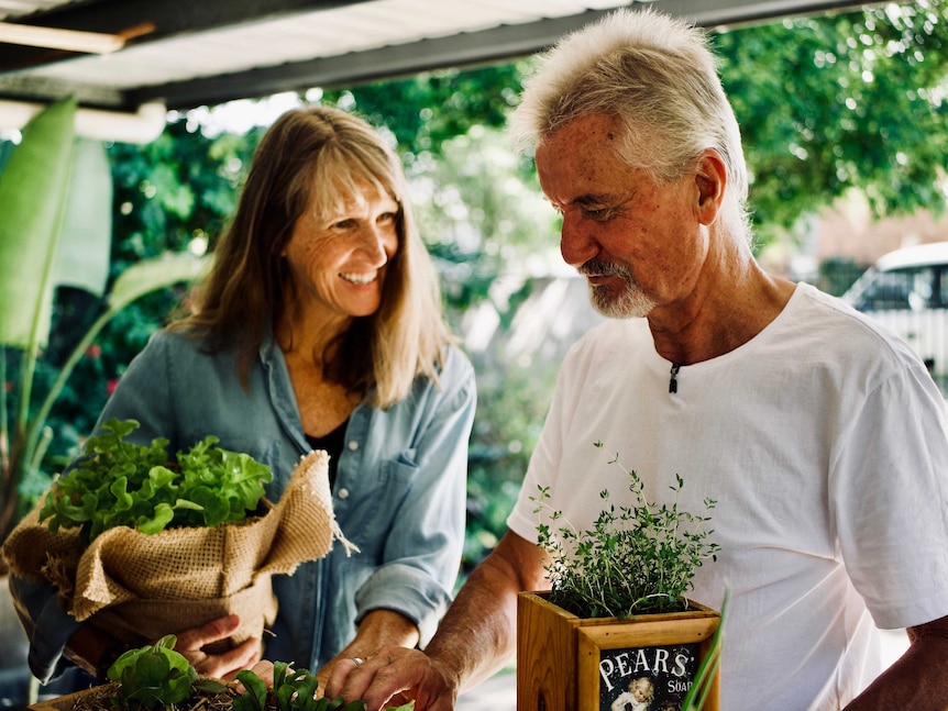 A woman and a man smile as they look at pot plants