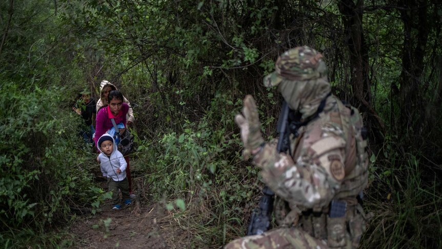 A man in heavy camouflage intercepts a family with young children in the woods