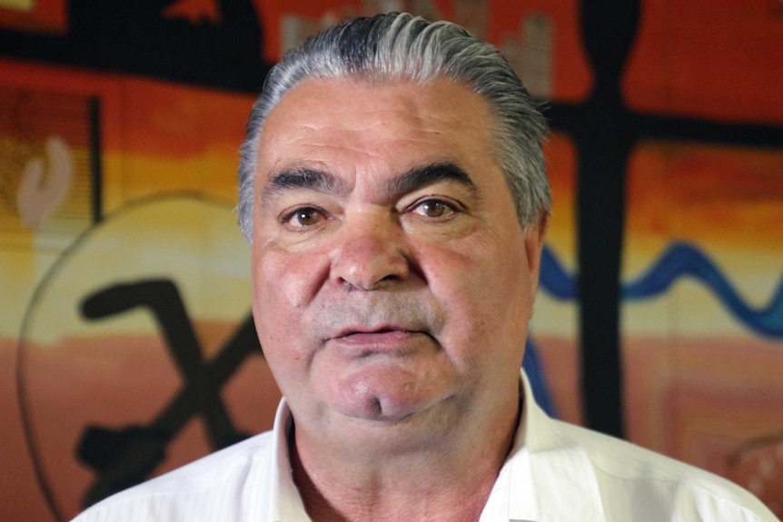 A head shot of Dennis Eggington with Aboriginal colours in the background.