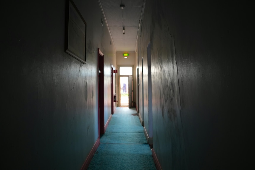 A dark hotel hallway with a light at the end of it. 