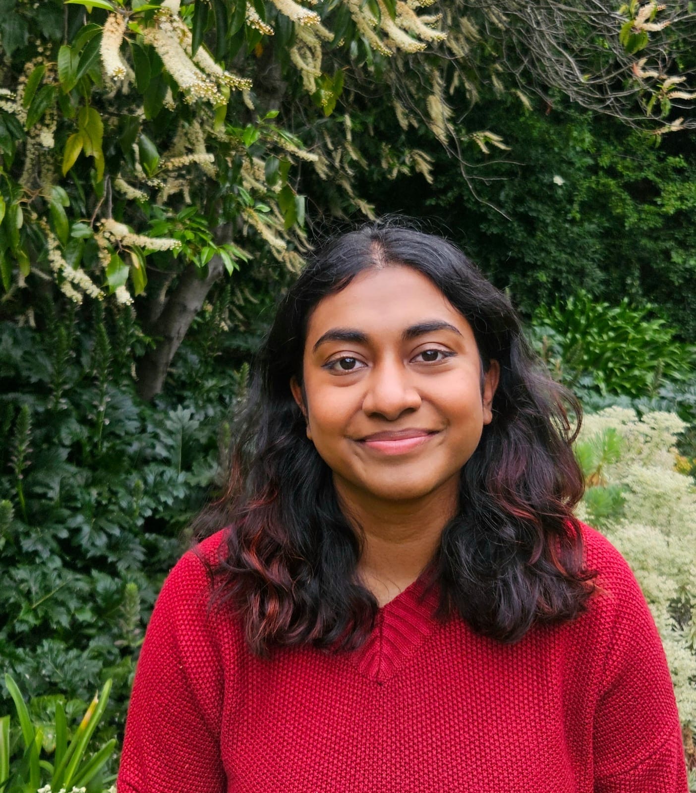 Una mujer con cabello oscuro y un suéter rojo sonríe.