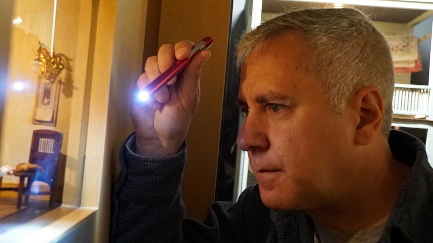 Veteran police detective Guy Olivieri trains his torch on the miniature crime scene display.
