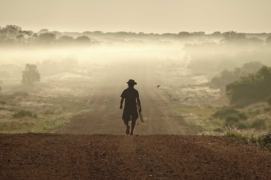 A silhouetted figure walks down a foggy road.