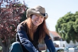 Woman in the garden wearing a hat, investigating the impact of using coffee grounds on plants.