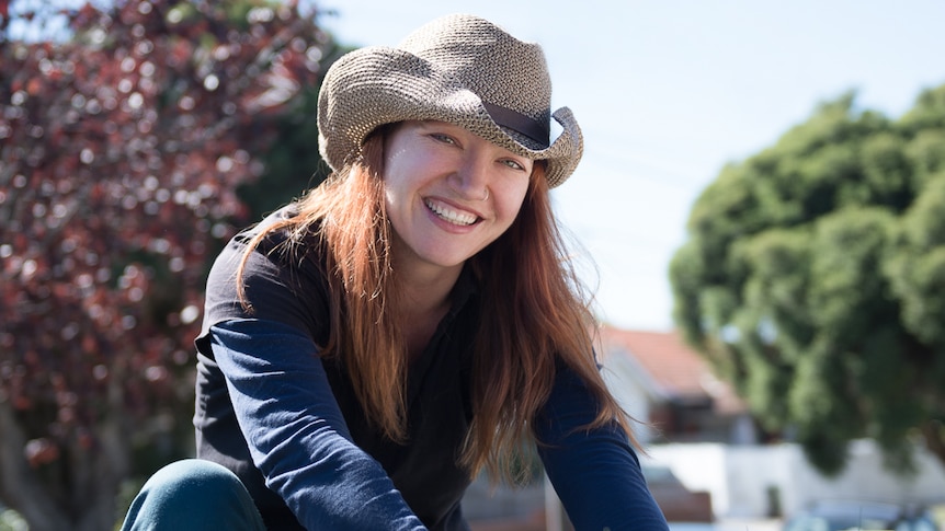 Woman in the garden wearing a hat, investigating the impact of using coffee grounds on plants.