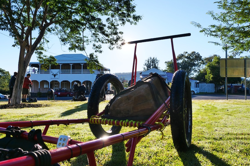 A rock on a cart rests on grass in front of a Queenslander-style building with a white verandah.