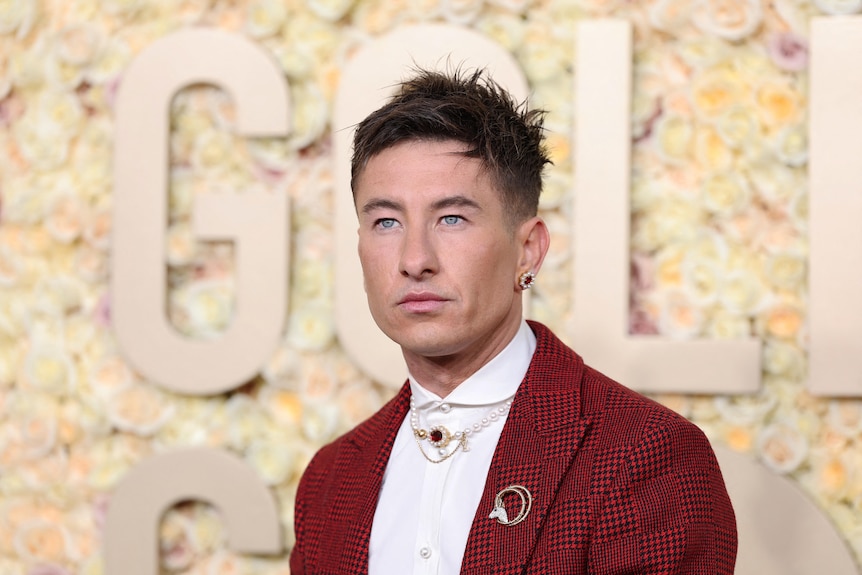 Barry poses with a steely face in a red-checked Louis Vuitton suit adorned with pearls, chains and a ruby earring