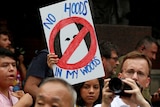 A woman holds up a sign with a cross through a KKK hood that says 'no hoods in my woods'.
