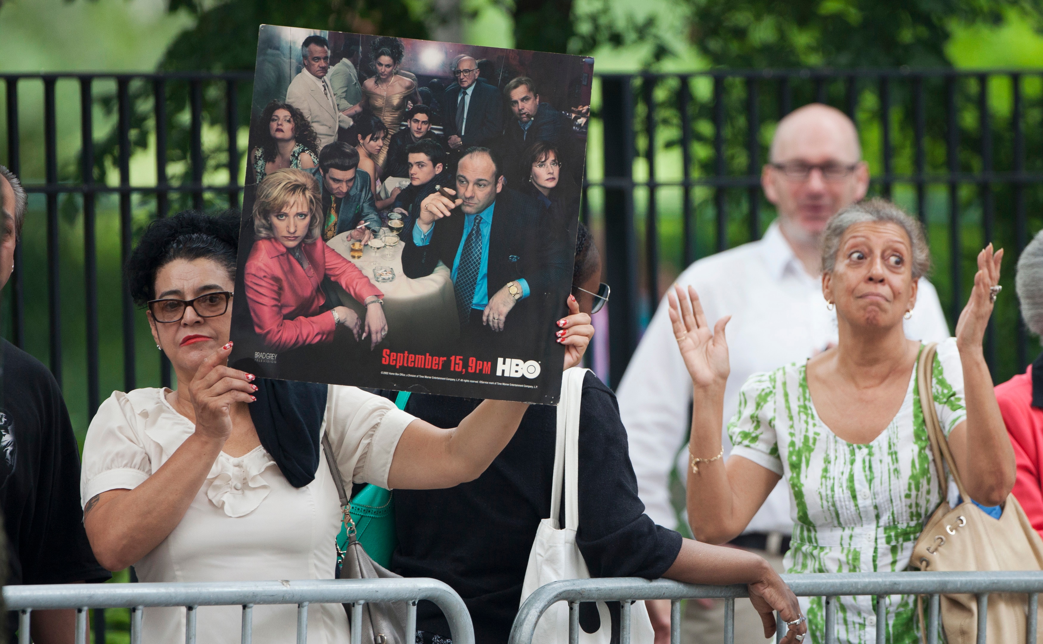 Uma mulher segura uma placa anunciando a série de televisão Os Sopranos atrás de uma barricada em uma rua.