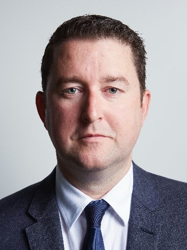 A head and shoulders photo of a man with short brown hair, wearing a blue suit jacket and tie.