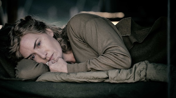 A woman in military attire lying on her side looking pensive