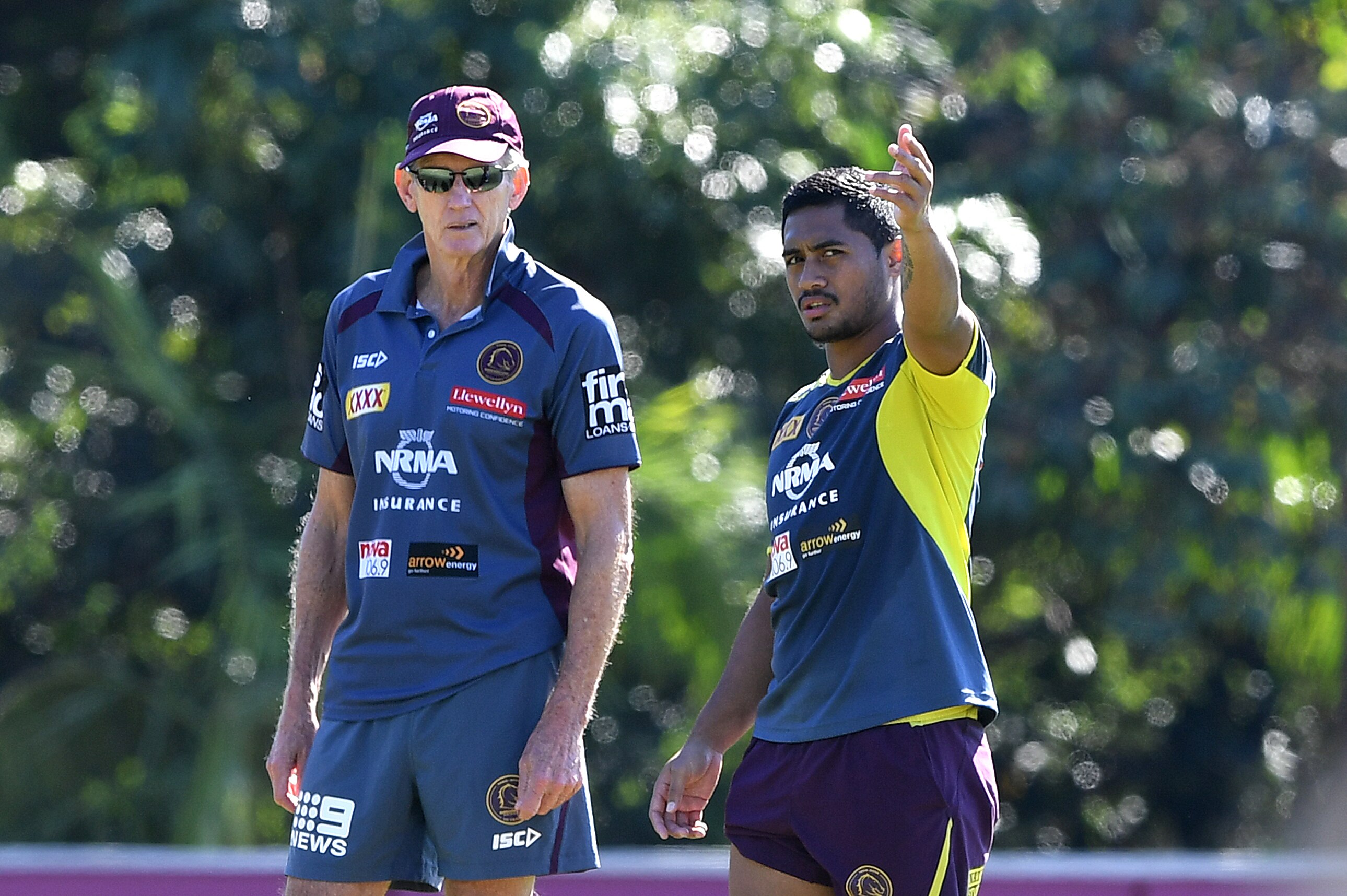 A Brisbane Broncos coach looks across a field as a player talks to him and points towards the action. 