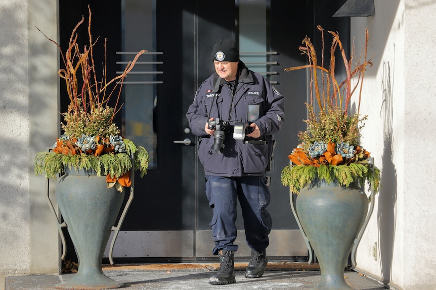 A police officer holding a camera at the steps of a home 