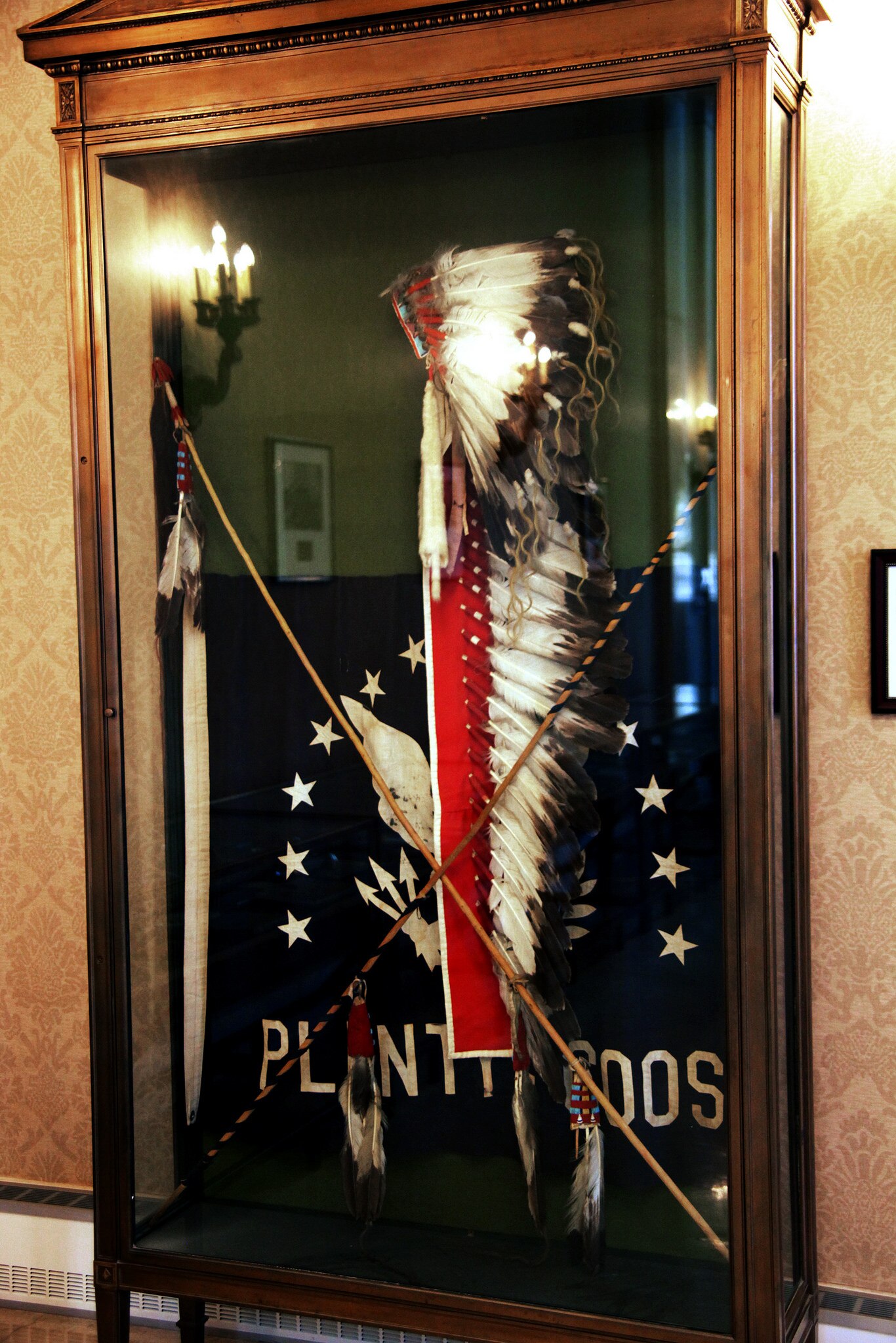 A feathered headdress and ceremonial stick in a glass cabinet