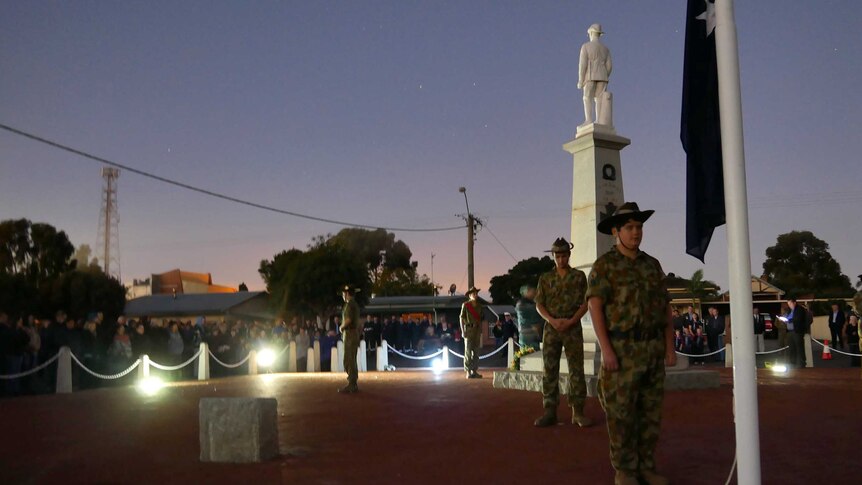 Soldiers stand around a war memorial and flagpole in the dawn light on Anzac Day.