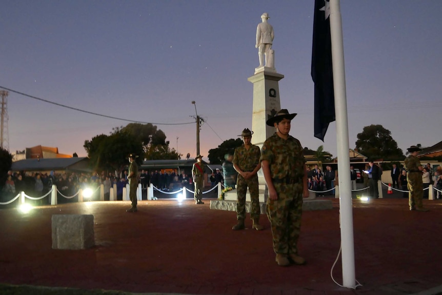 Soldiers stand around a war memorial and flagpole in the dawn light on Anzac Day.