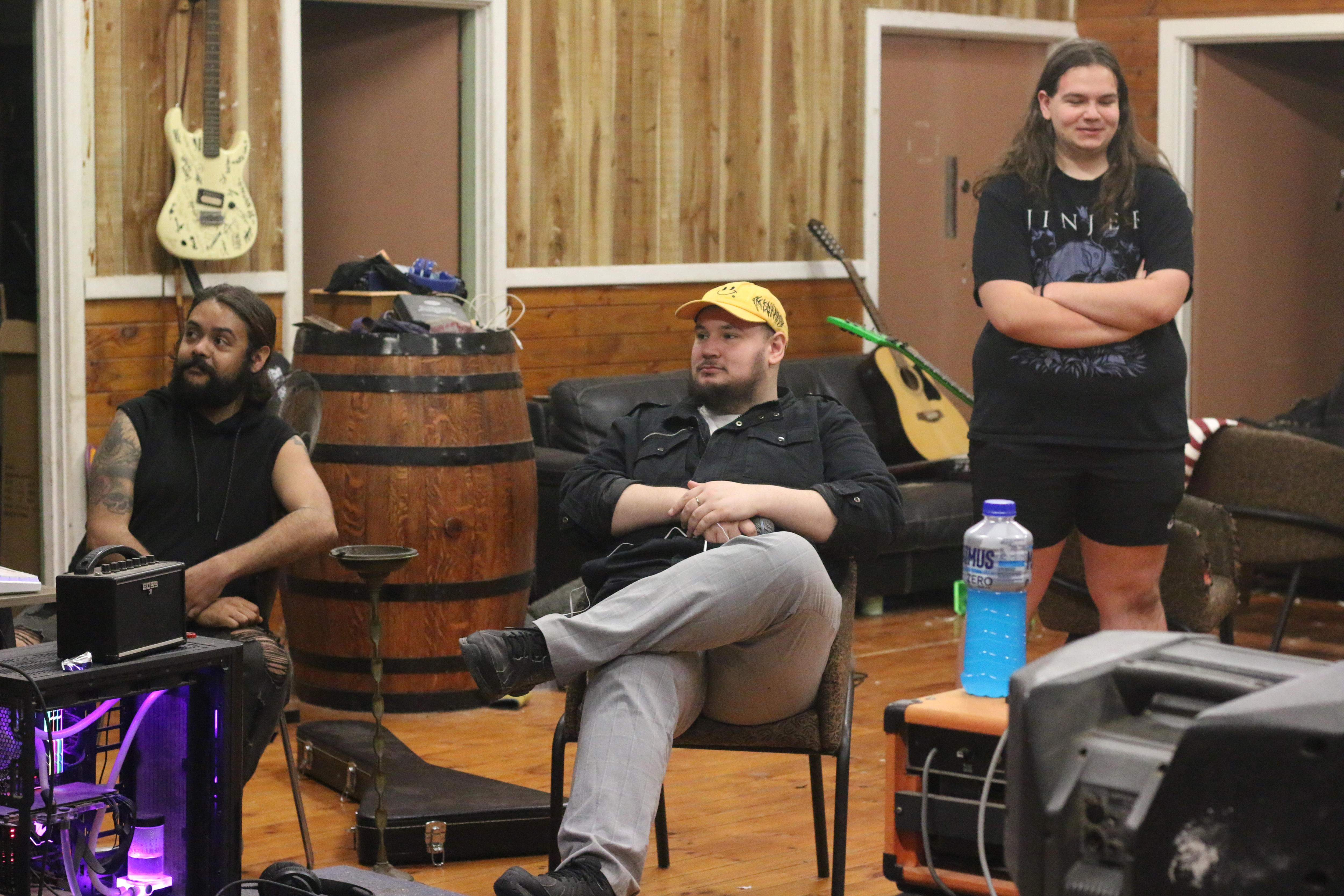 Três homens reunidos em uma sala comunitária. 