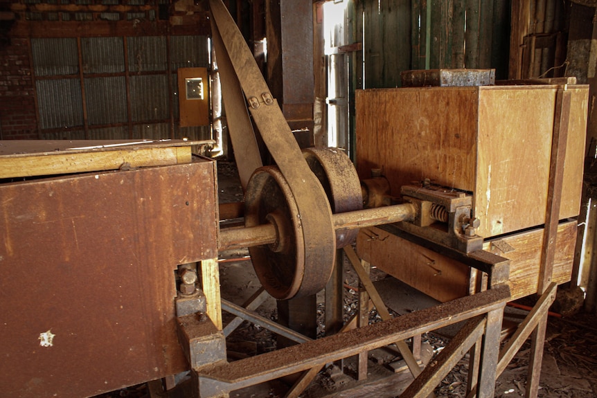 Old wooden machinery with a wheel and a belt wrapped around it.