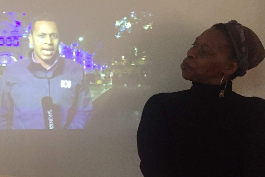 Woman looking sideways at image projected on wall of reporter holding ABC News microphone.