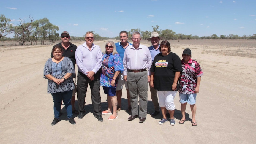 Menindee locals and politicians pose for a photo standing in the centre of an unsealed road near Menindee.