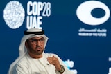 A man wearing a Ghutra sits and speaks in front of a backdrop with the 'COP28UAE' logo