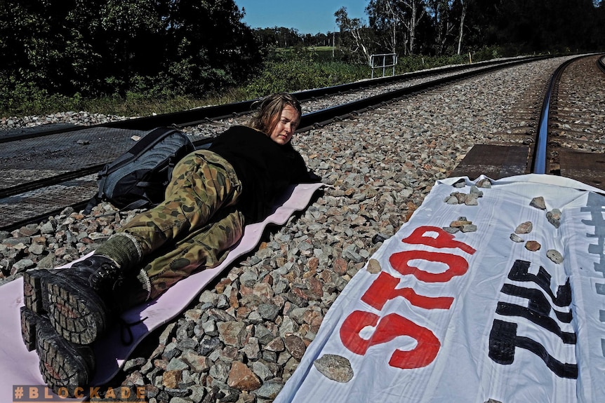 A woman lays on a a train train with a sign that reds ' stop the machine'.