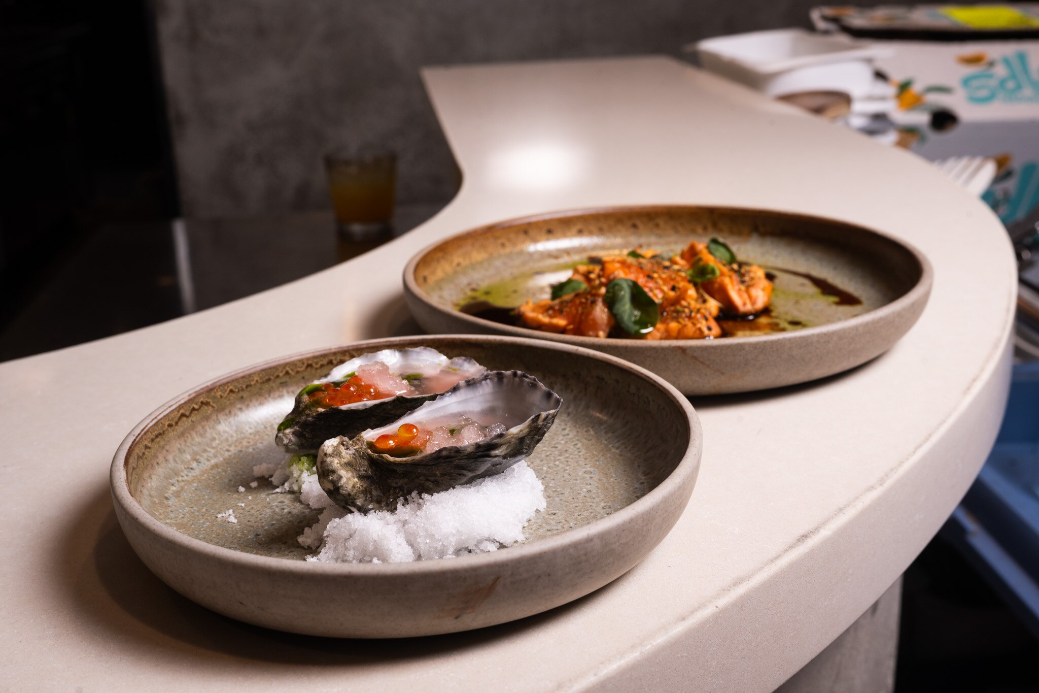A close up of oysters on a plate with granita and roe, and another dish with orange coloured sauce and green leaves to garnish.