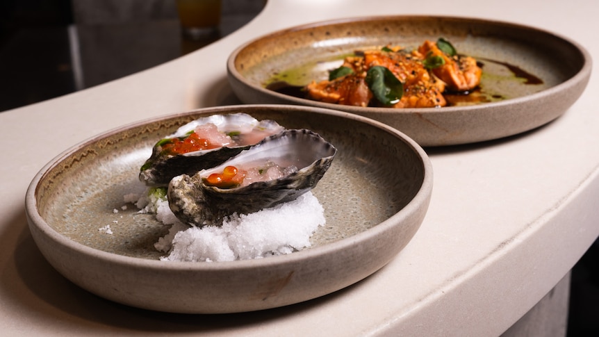 A close up of oysters on a plate with granita and roe, and another dish with orange coloured sauce and green leaves to garnish.