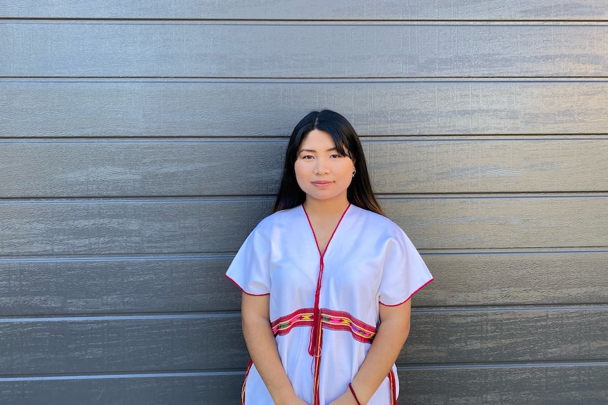 Paw Ku Htee poses for a photo, wearing a white shirt with a red lining. 