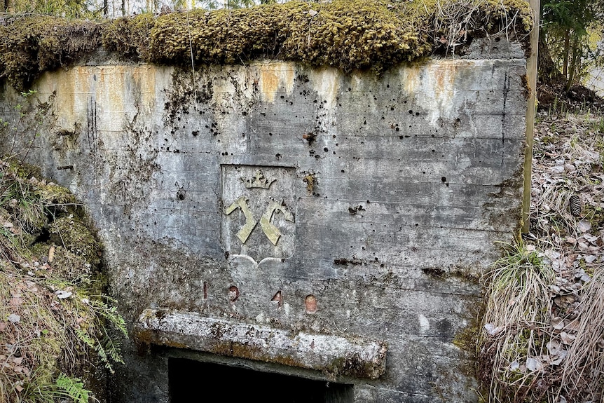 An emblem engraved into the top of a bunker showing two different hands holding swords.