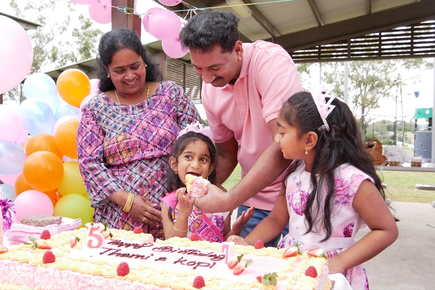 A young girl eats a slice of birthday cake surrounded by her family