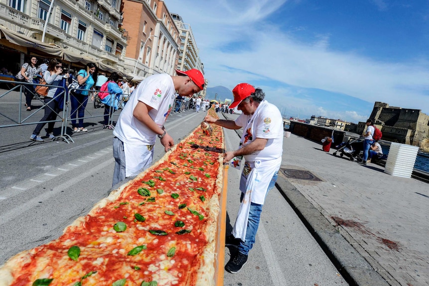 View looking down the pizza of two pizza makers adding topping to the pizza.